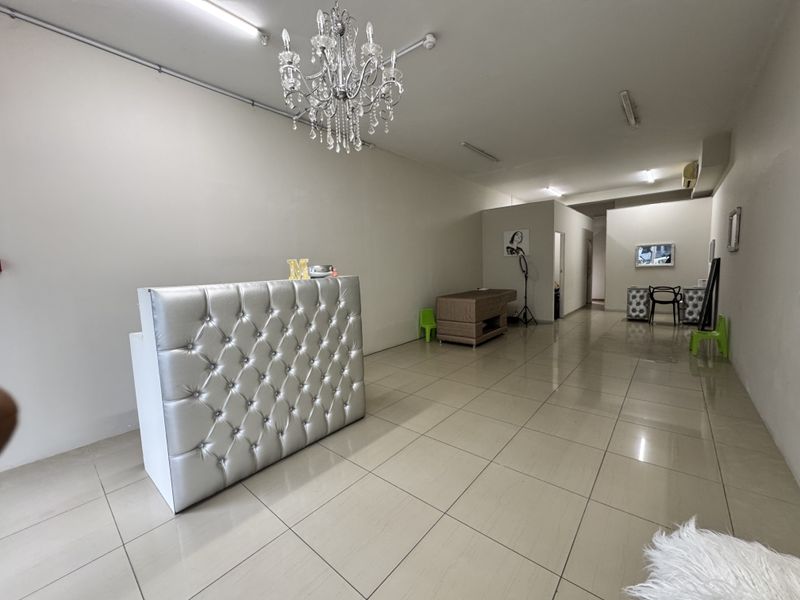 Open-plan retail or salon space featuring neutral walls, large format floor tiles, and a decorative crystal chandelier.