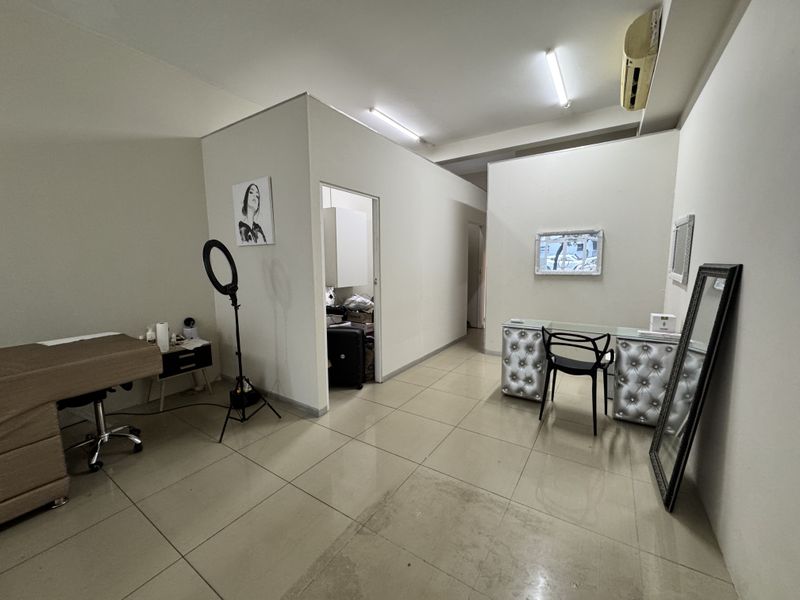 A functional commercial utility space featuring tiled flooring, split-system air conditioning, and overhead fluorescent lighting, suitable for a salon or office environment.