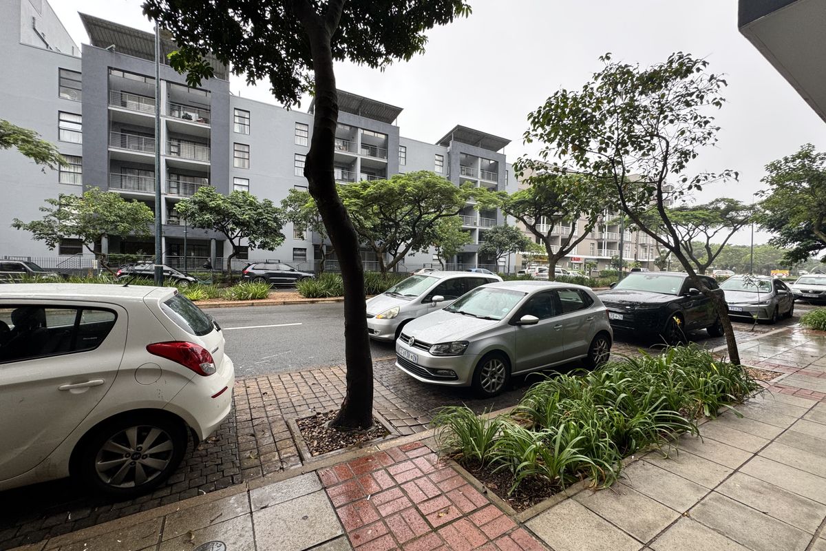 Street-level view of a multi-story residential complex featuring paved sidewalks, landscaped verges, and building facades with balconies.