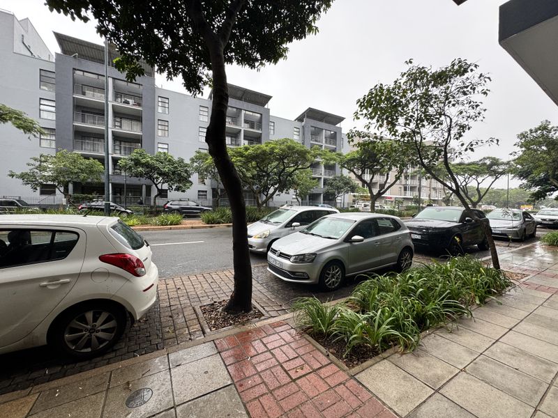 Street-level view of a multi-story residential complex featuring paved sidewalks, landscaped verges, and building facades with balconies.