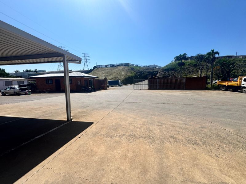 Spacious industrial yard featuring a concrete surface, covered parking area, and secure gated access point.