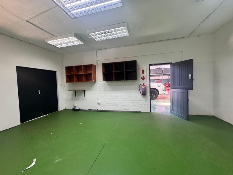 A clean, functional utility space featuring painted concrete flooring, built-in wall shelving, and fluorescent lighting, suitable for storage or workshop use.