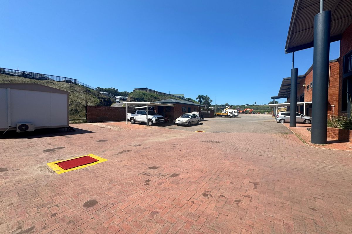 Spacious industrial paved yard area featuring a covered carport, brick boundary walls, and steel structural supports under a clear blue sky.