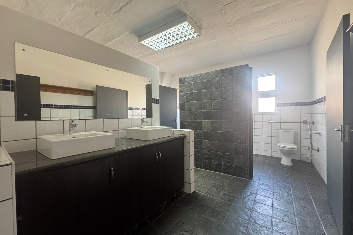 Spacious industrial-style bathroom featuring a double vanity with stone countertop, dark cabinetry, tiled flooring, and accessible grab rails.