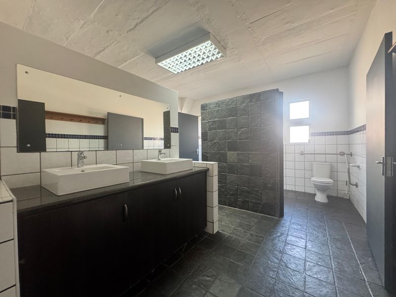 Spacious industrial-style bathroom featuring a double vanity with stone countertop, dark cabinetry, tiled flooring, and accessible grab rails.