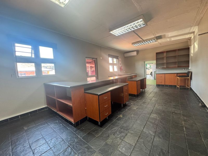 Spacious industrial office area featuring built-in cabinetry, tiled flooring, split-system air conditioning, and ample natural light through security-barred windows.
