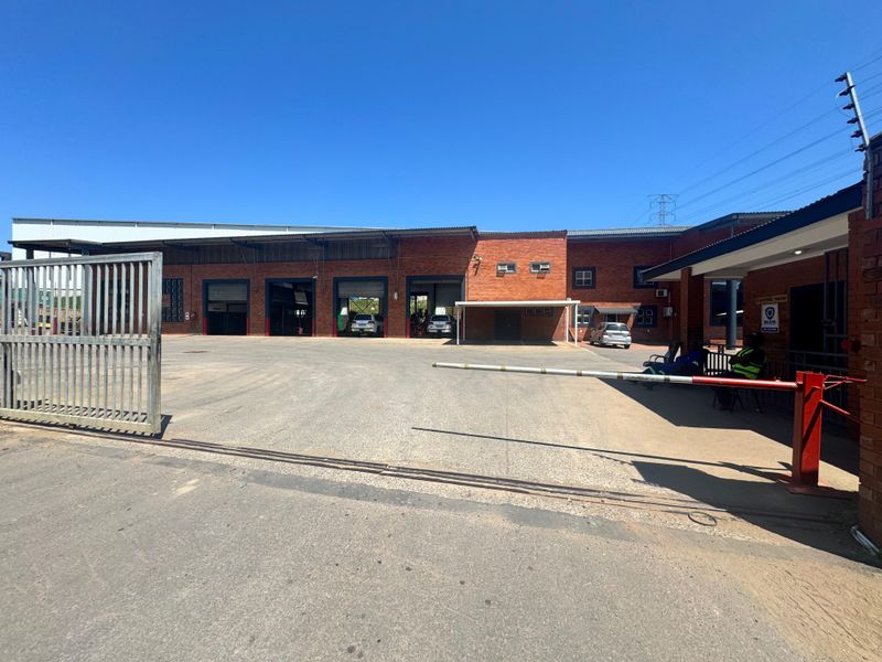 Industrial property exterior featuring a secure gated entrance, asphalt driveway, and multiple roller shutter bays with brick facade construction.