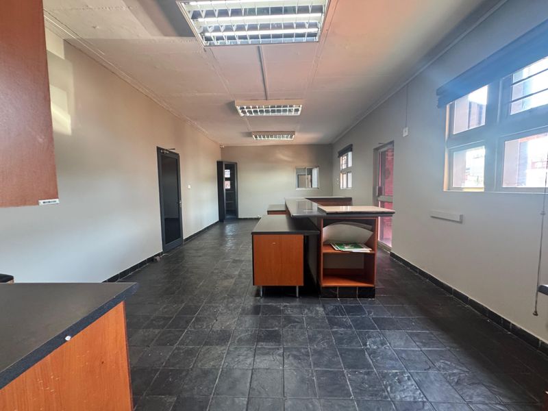 Spacious open-plan industrial office or utility area featuring tiled flooring, built-in cabinetry, and recessed fluorescent lighting.