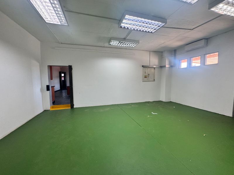 An empty industrial utility space featuring a painted concrete floor, suspended ceiling with fluorescent lighting, and a wall-mounted air conditioning unit.