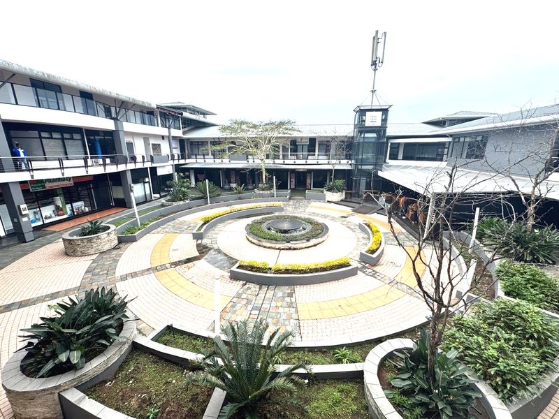 A central courtyard featuring a circular paved design, a water fountain, and landscaped planters surrounded by a multi-level office building complex.