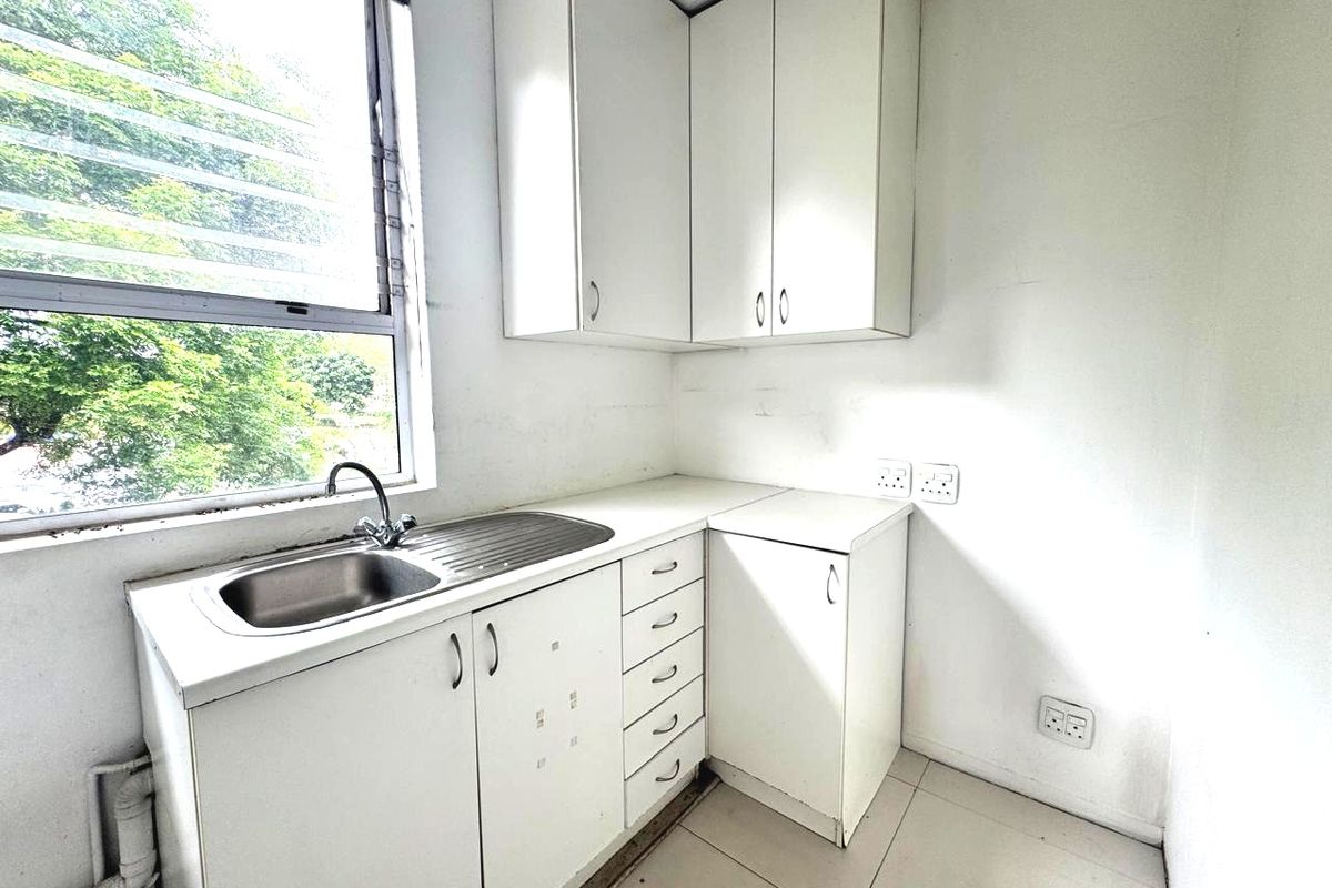 A compact kitchenette featuring white built-in cabinetry, a stainless steel sink, and tiled flooring, suitable for a small office or utility space.