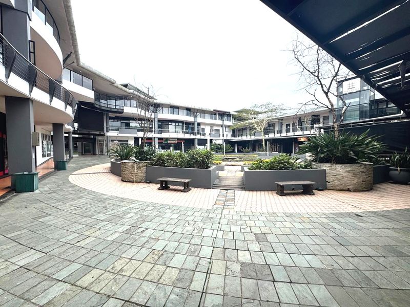 A spacious, paved central courtyard within a multi-level office complex, featuring raised garden beds and modern architectural design.