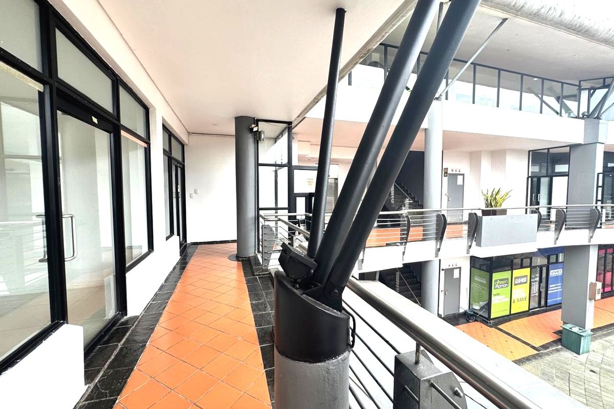 An elevated outdoor walkway or balcony area featuring tiled flooring, metal safety railings, and structural support columns within a commercial office complex.