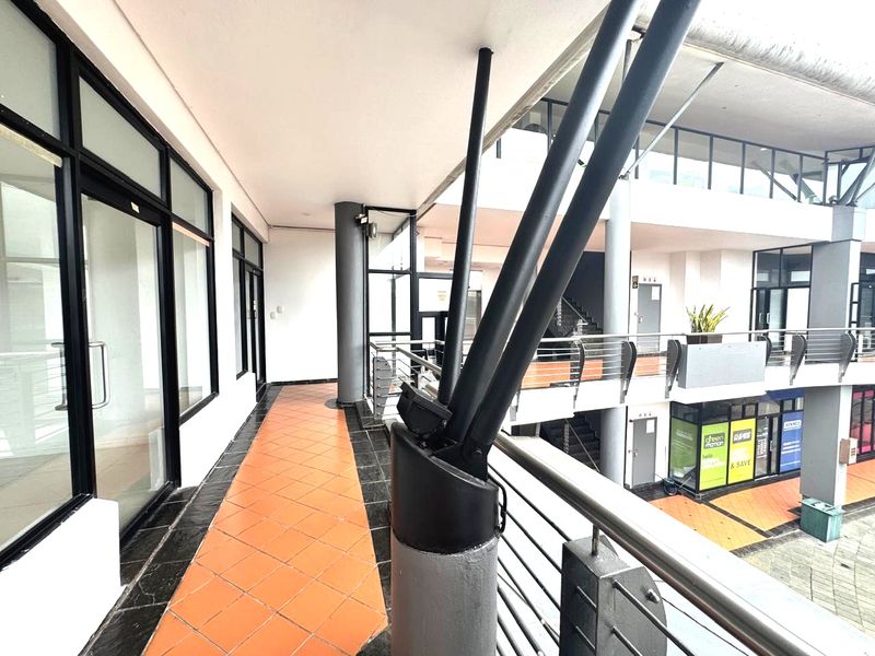 An elevated outdoor walkway or balcony area featuring tiled flooring, metal safety railings, and structural support columns within a commercial office complex.