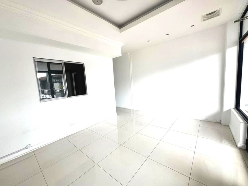 A bright, empty office space featuring clean tiled flooring, recessed ceiling lighting, and a large window providing natural light.