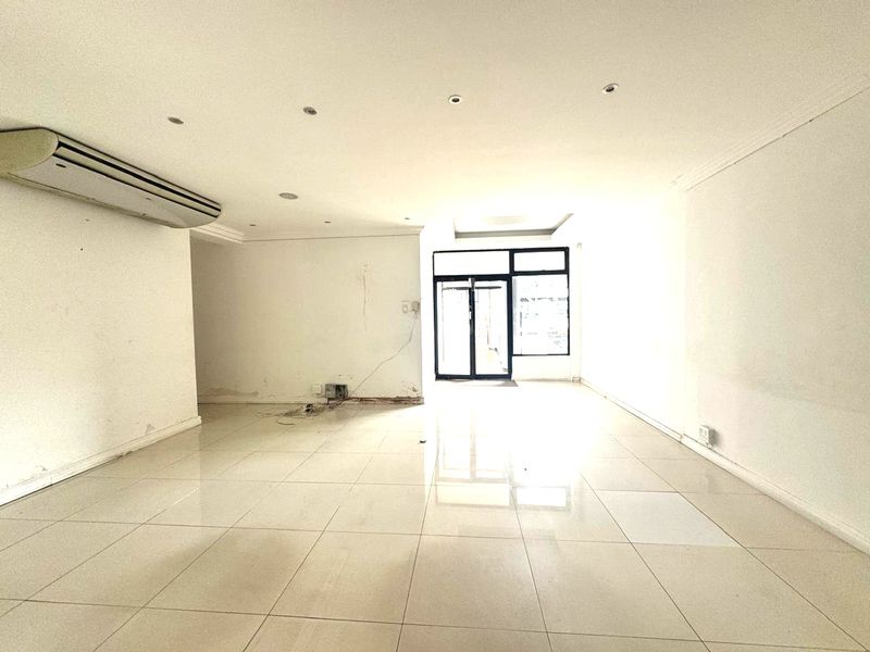 An empty, open-plan office space featuring tiled flooring, recessed lighting, and a wall-mounted air conditioning unit, ready for custom fit-out.