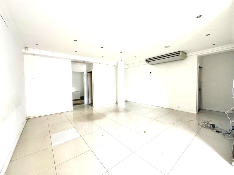 An empty, open-plan office space featuring tiled flooring, recessed ceiling lighting, and a wall-mounted air conditioning unit.