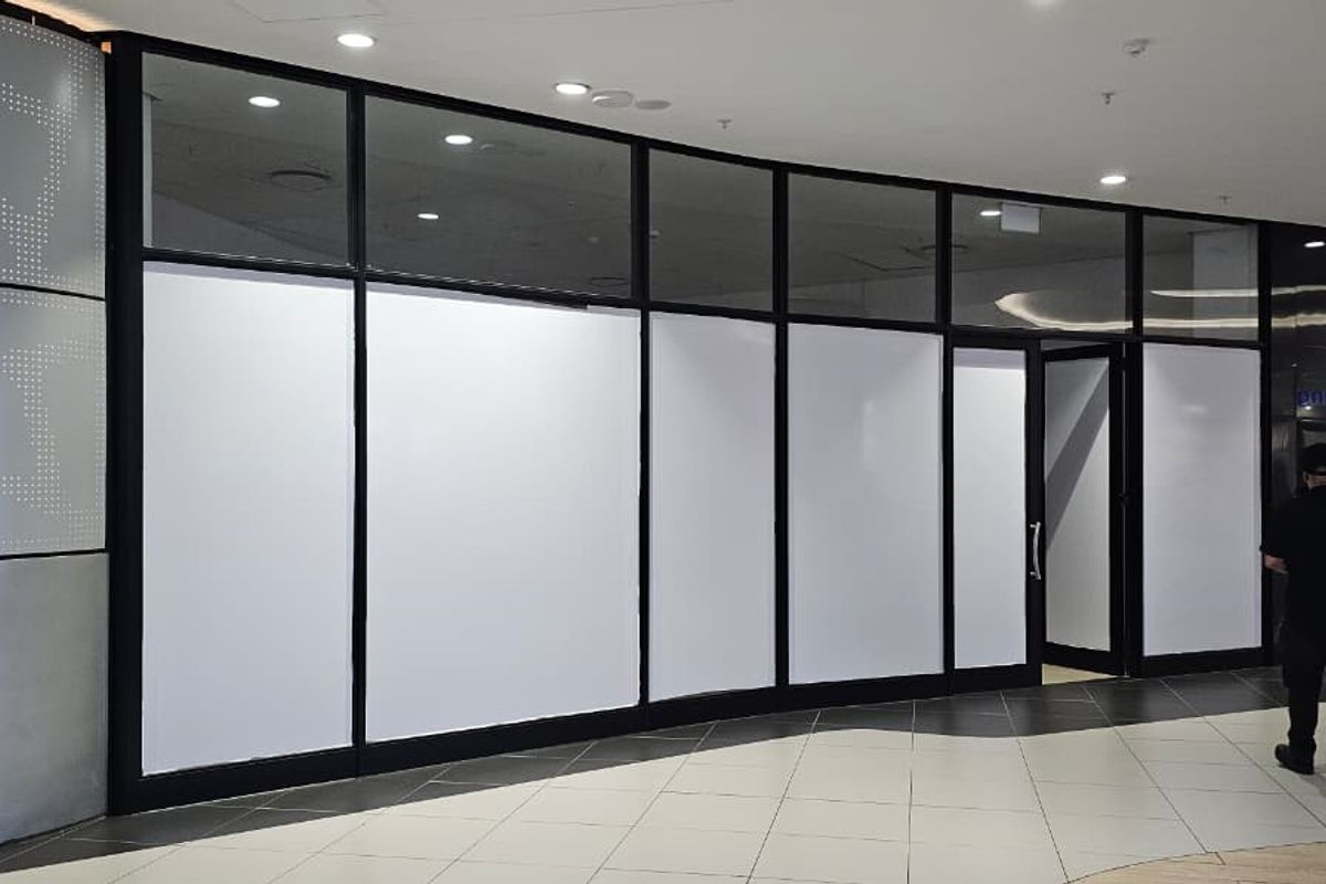 A vacant retail storefront featuring a modern glass facade with metal framing, recessed lighting, and tiled flooring in a shopping mall setting.