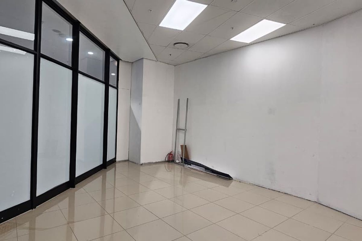 Empty open-plan retail space featuring tiled flooring, suspended ceiling with recessed lighting, and a modern glass partition wall.