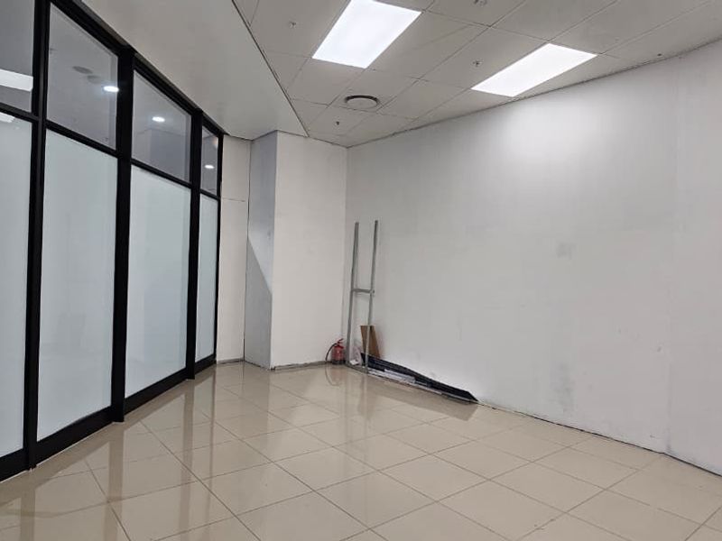 Empty open-plan retail space featuring tiled flooring, suspended ceiling with recessed lighting, and a modern glass partition wall.
