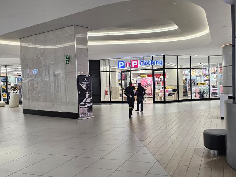 A modern, well-lit retail mall corridor featuring polished tiled flooring, marble-clad structural pillars, and glass-fronted retail units.