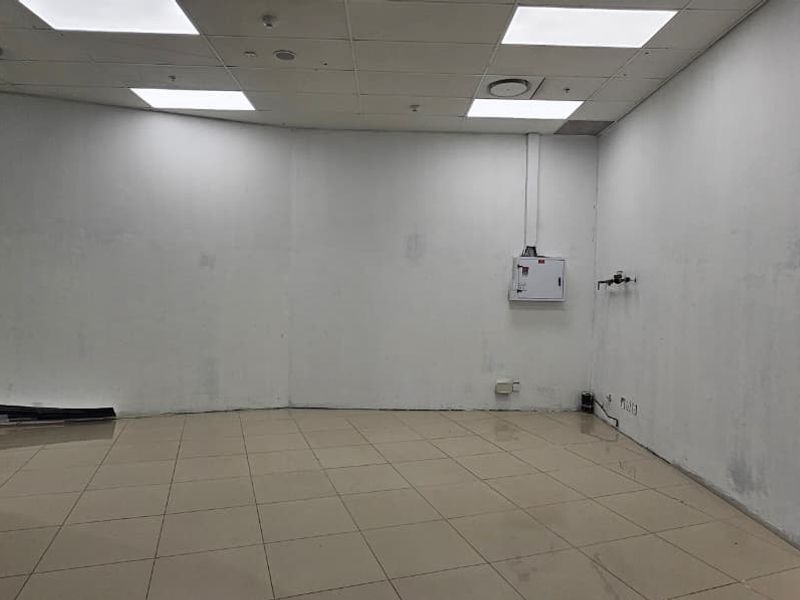 An empty retail utility space featuring ceramic tile flooring, a suspended ceiling with recessed lighting, and basic electrical and plumbing infrastructure.