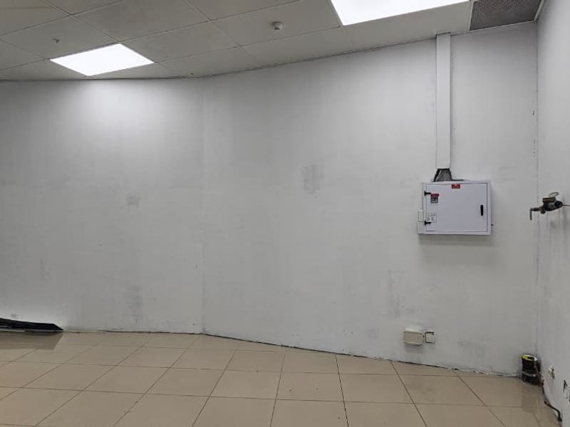 An empty retail utility space featuring tiled flooring, recessed ceiling lights, and wall-mounted electrical infrastructure, suitable for various commercial storage or operational uses.