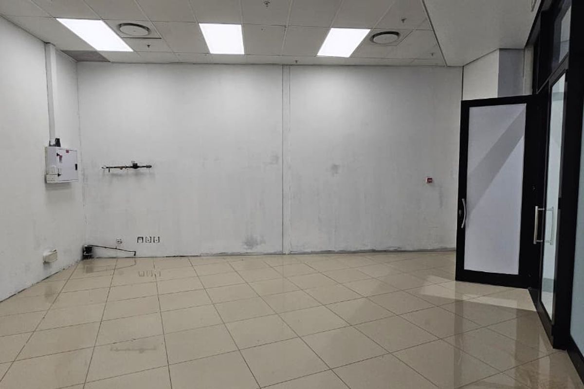 An empty retail or office space featuring tiled flooring, a suspended ceiling with recessed lighting, and a glass entrance door.