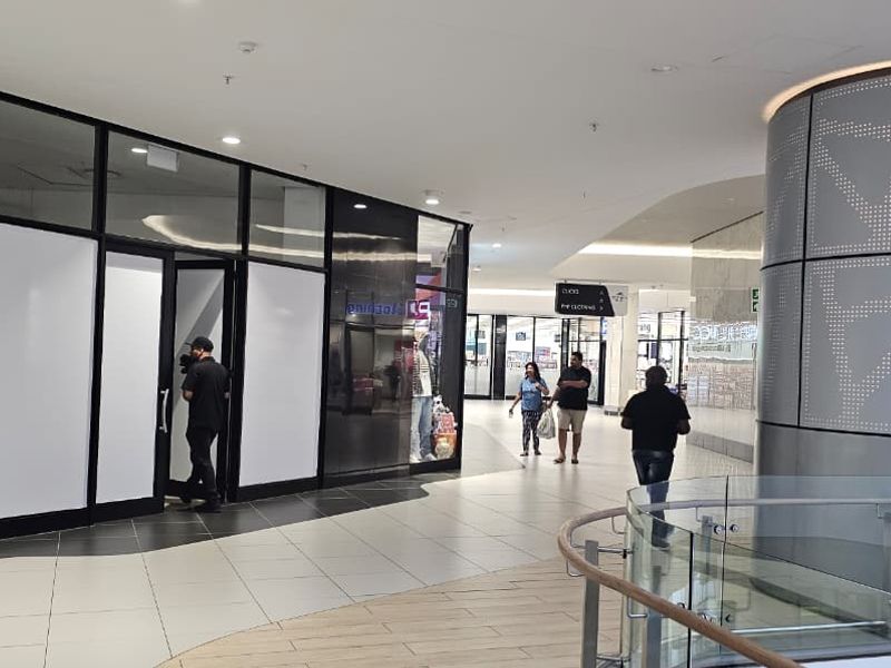 A modern retail storefront entrance within a shopping center, featuring glass paneling, tiled floors, and contemporary architectural finishes.