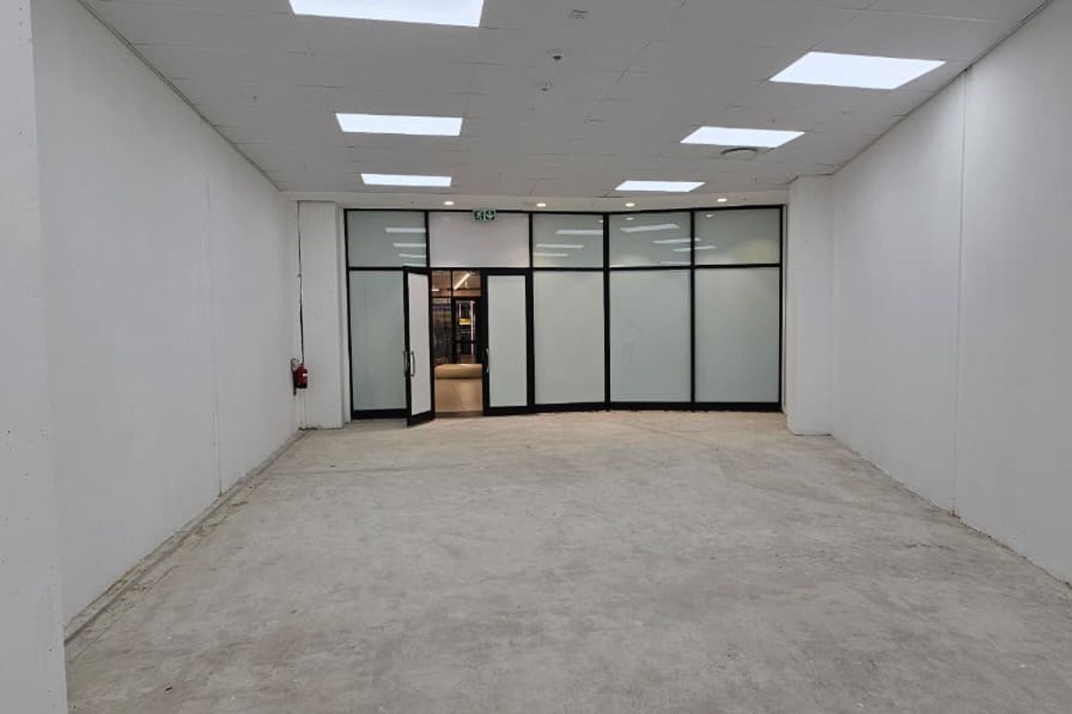 An empty, open-plan retail space featuring a suspended ceiling with recessed lighting and a large glass storefront entrance.