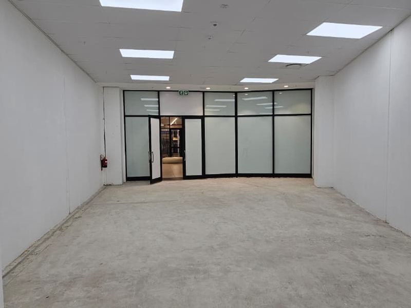 An empty, open-plan retail space featuring a suspended ceiling with recessed lighting and a large glass storefront entrance.
