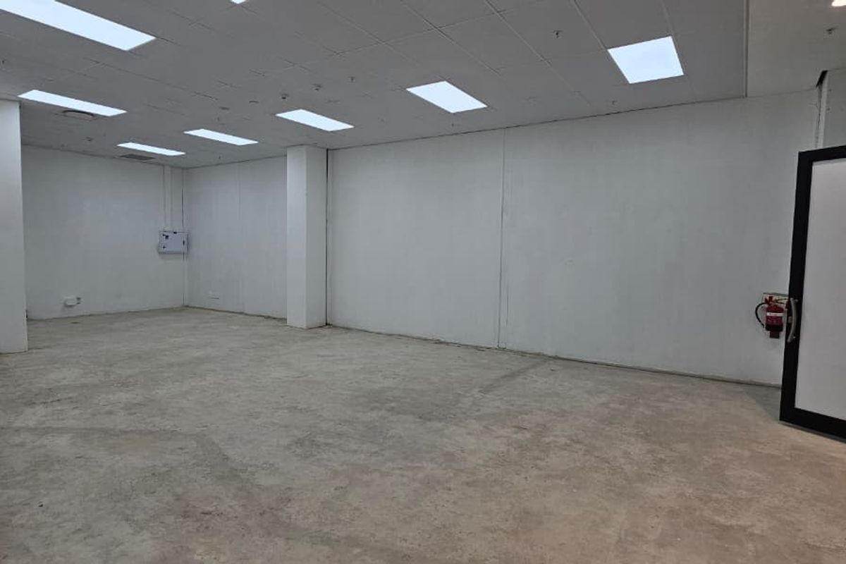 An empty, open-plan retail space featuring a suspended ceiling with recessed lighting, concrete flooring, and a glass entrance door.