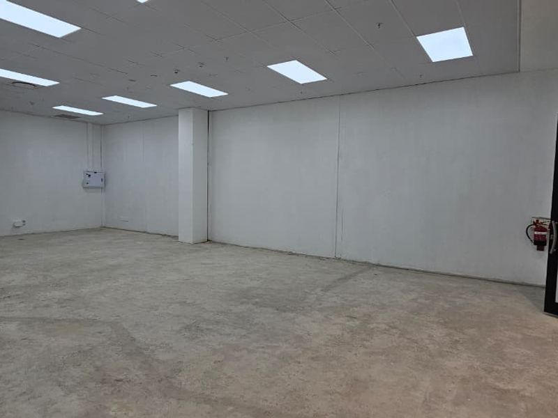 An empty, open-plan retail space featuring a suspended ceiling with recessed lighting, concrete flooring, and a glass entrance door.
