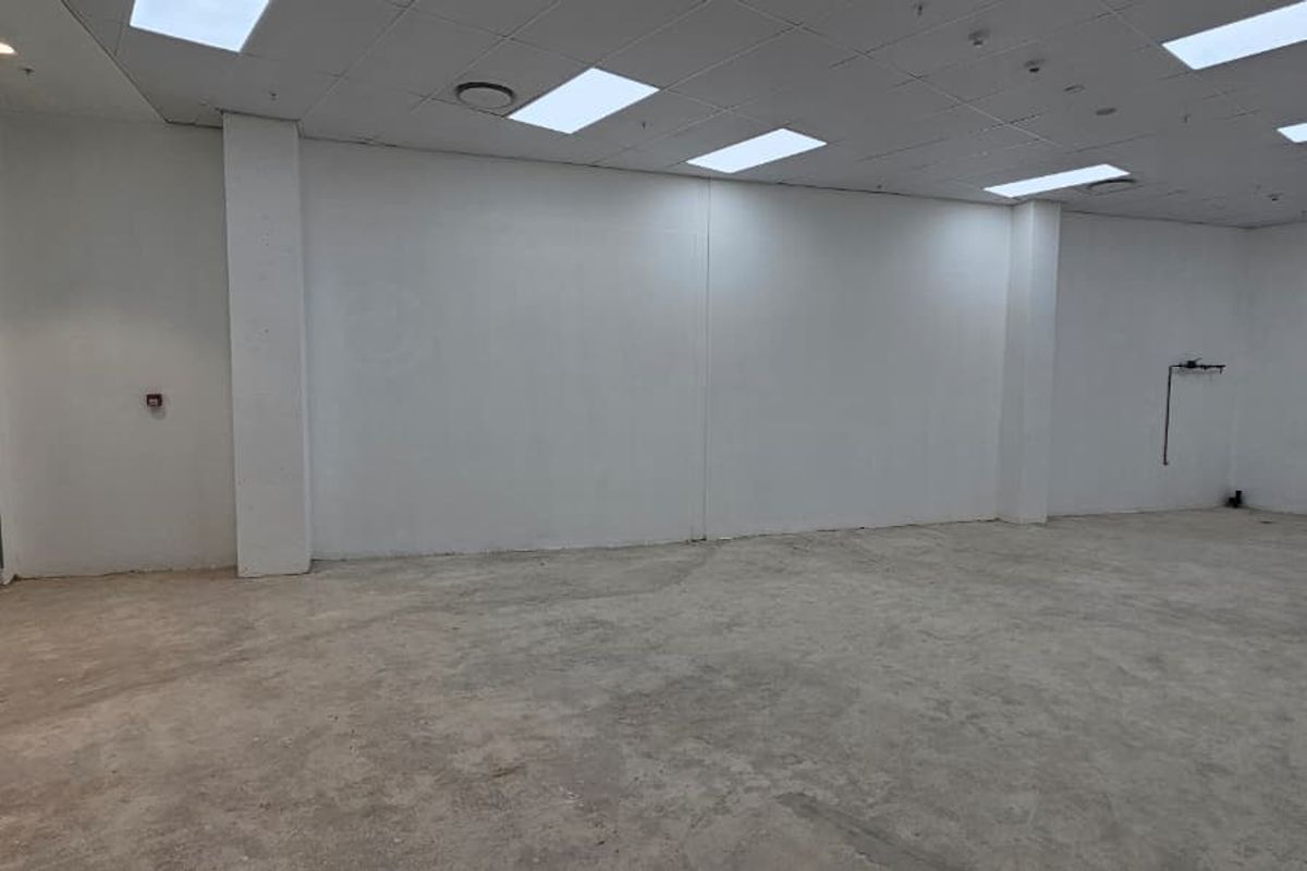 A vacant, open-plan retail space featuring a suspended ceiling, recessed lighting, and an unfinished concrete floor, ready for custom fit-out.