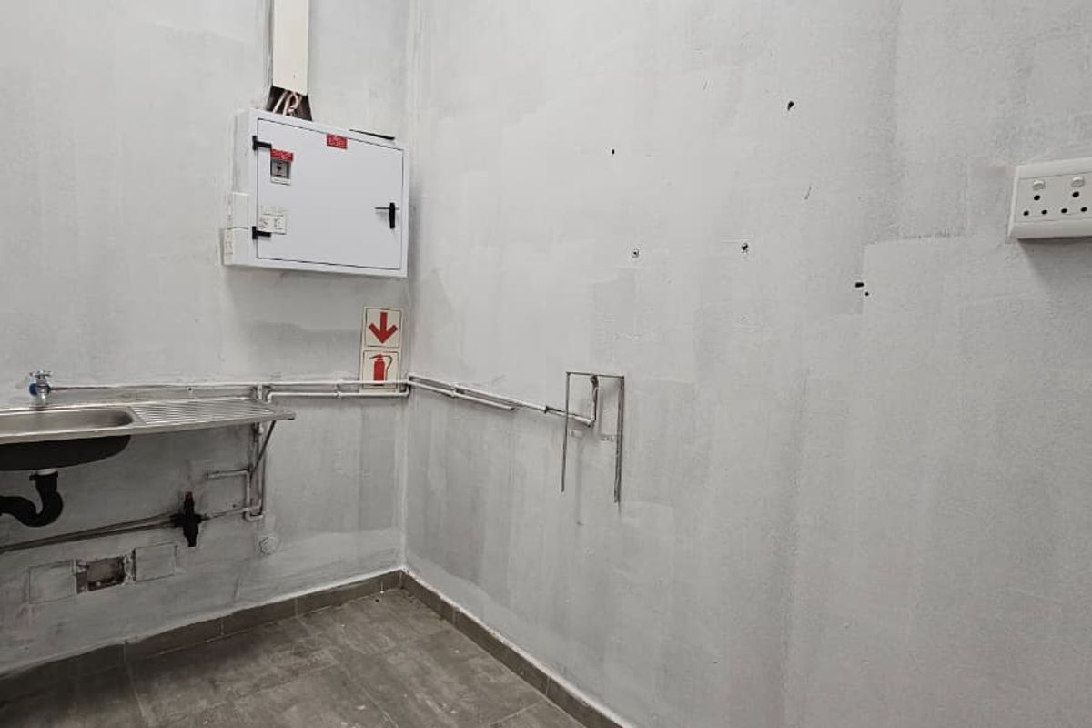 A functional utility or laundry space featuring a stainless steel sink, exposed plumbing, and an electrical distribution board, ready for final finishing.