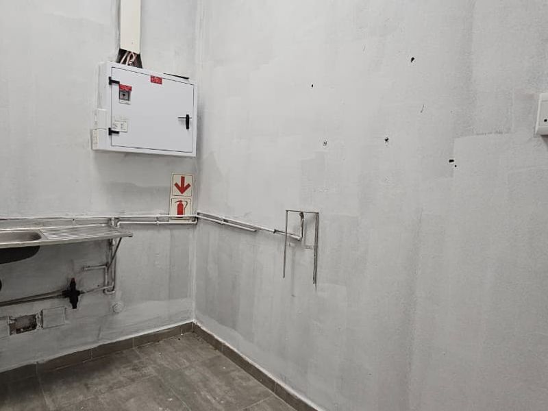 A functional utility or laundry space featuring a stainless steel sink, exposed plumbing, and an electrical distribution board, ready for final finishing.