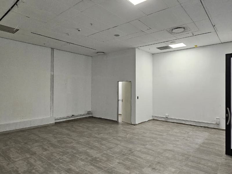 An empty, open-plan retail space featuring tiled flooring, a suspended ceiling with recessed lighting, and a glass entrance door.