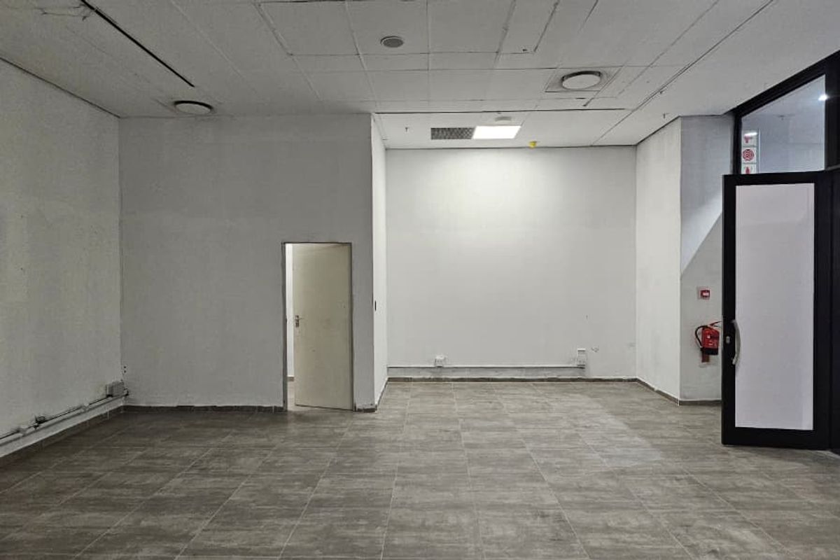 An empty retail space featuring tiled flooring, a suspended ceiling with recessed lighting, and a glass entrance door leading to a mall corridor.