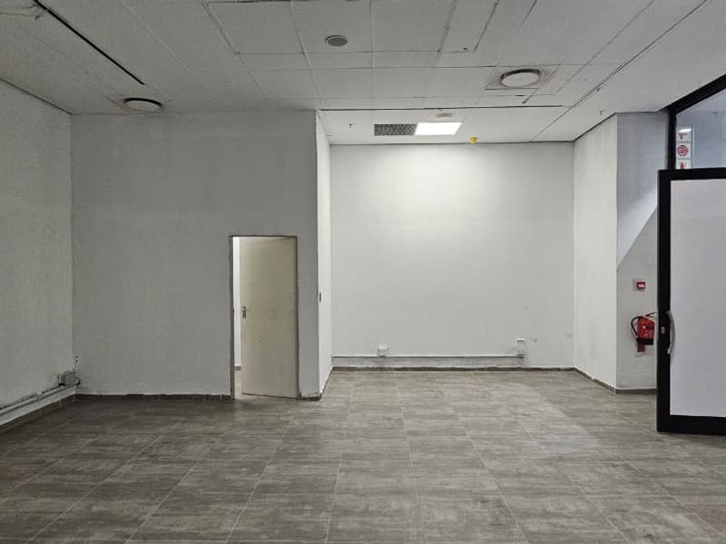 An empty retail space featuring tiled flooring, a suspended ceiling with recessed lighting, and a glass entrance door leading to a mall corridor.