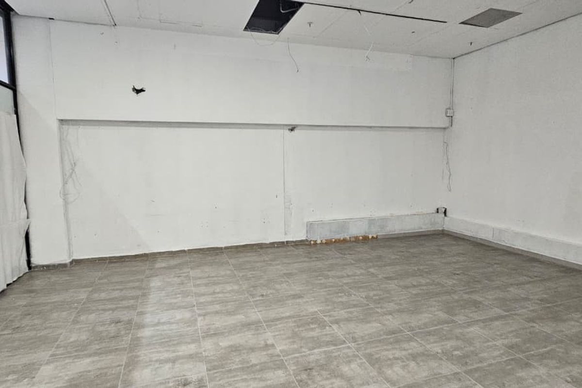 An empty, open-plan retail space featuring tiled flooring and a large storefront window, currently requiring ceiling and wall repairs.