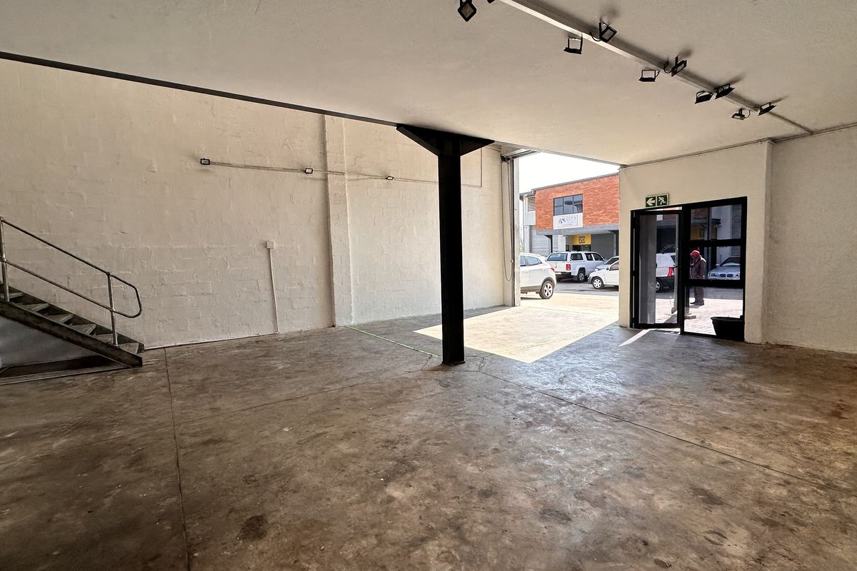 Open-plan industrial utility space featuring concrete flooring, a steel staircase, and track lighting, with direct access to the exterior parking area.