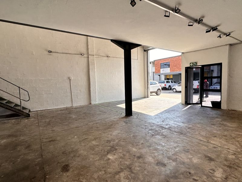 Open-plan industrial utility space featuring concrete flooring, a steel staircase, and track lighting, with direct access to the exterior parking area.