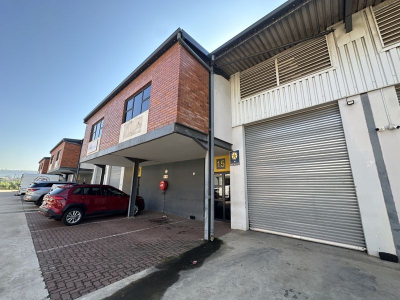 Industrial unit featuring a large roller shutter door, brick and metal facade, and dedicated paved parking area in a secure business park setting.