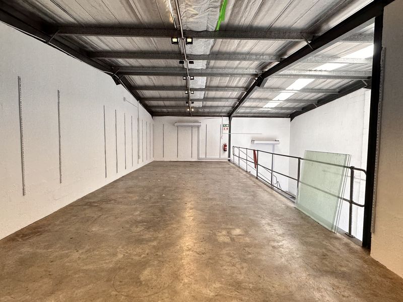 Spacious industrial mezzanine level featuring exposed steel roof structure, concrete flooring, and wall-mounted shelving tracks, suitable for storage or flexible workspace.