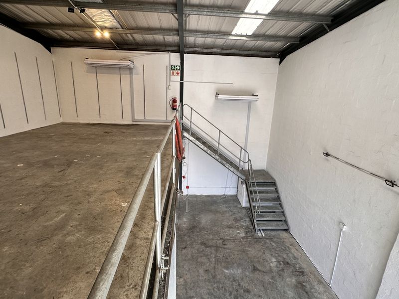 Industrial utility space featuring a mezzanine level, metal staircase, exposed steel roof structure, and concrete flooring, suitable for storage or workshop use.