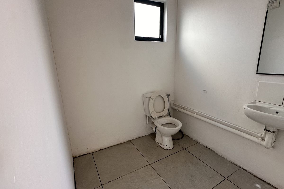 A functional, minimalist bathroom featuring a toilet, wall-mounted basin, and tiled flooring, currently in need of cosmetic updates and finish improvements.