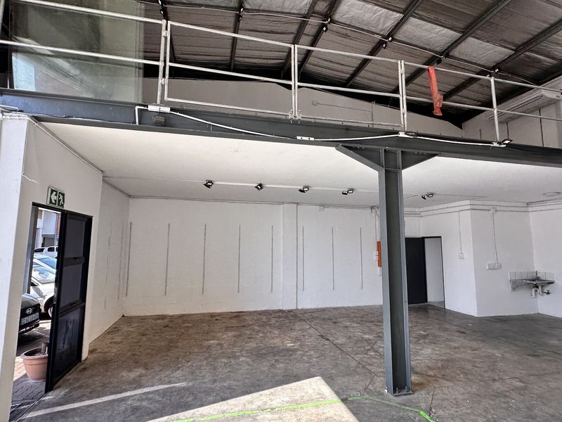Spacious industrial utility area featuring a mezzanine level, exposed steel structural elements, concrete flooring, and a functional wall-mounted sink.