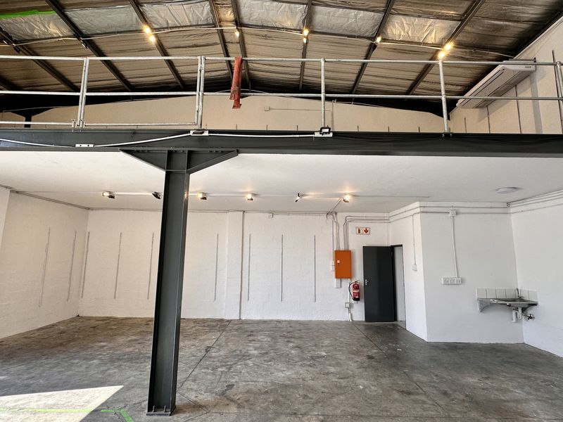 Open-plan industrial utility space featuring a mezzanine level, exposed roof structure, concrete flooring, and a small wall-mounted sink.