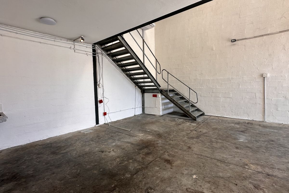 Industrial utility space featuring a metal staircase, concrete flooring, and a wall-mounted sink, suitable for workshop or storage use.