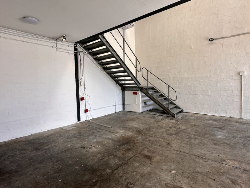 Industrial utility space featuring a metal staircase, concrete flooring, and a wall-mounted sink, suitable for workshop or storage use.